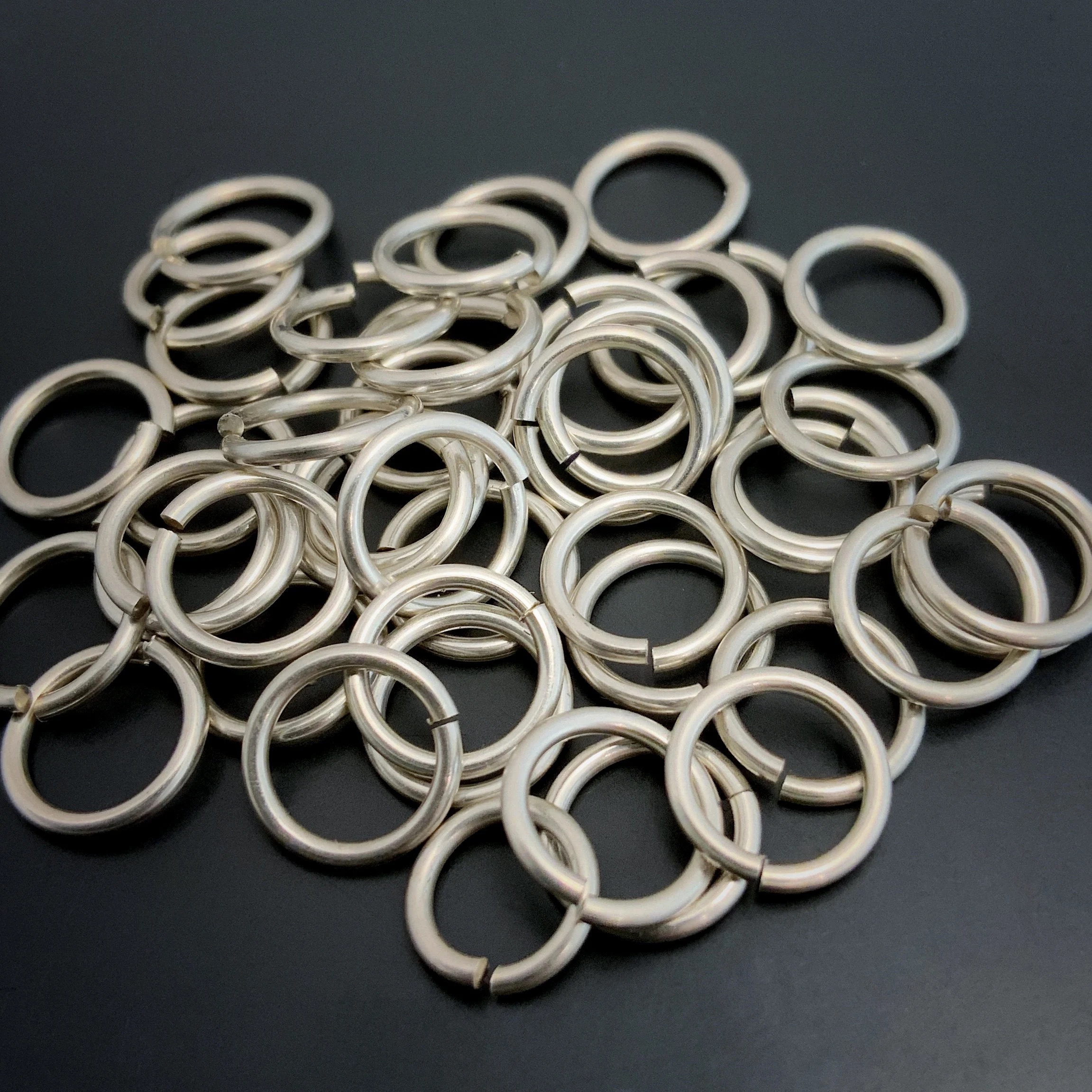 Pile of jump rings shown against a dark background. They are shiny, smooth, and open.