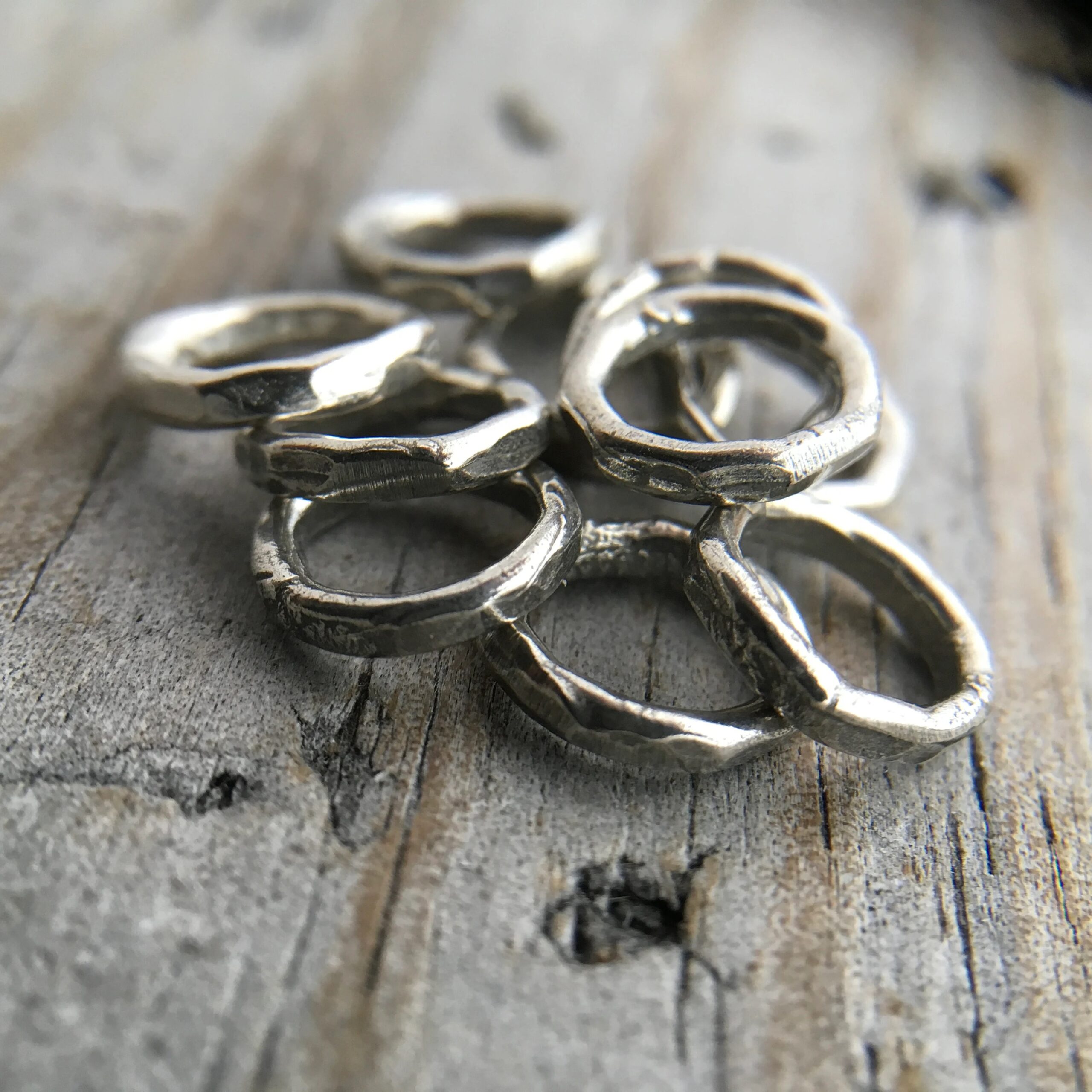 Pile of soldered oxidized jump rings against a wooden background.