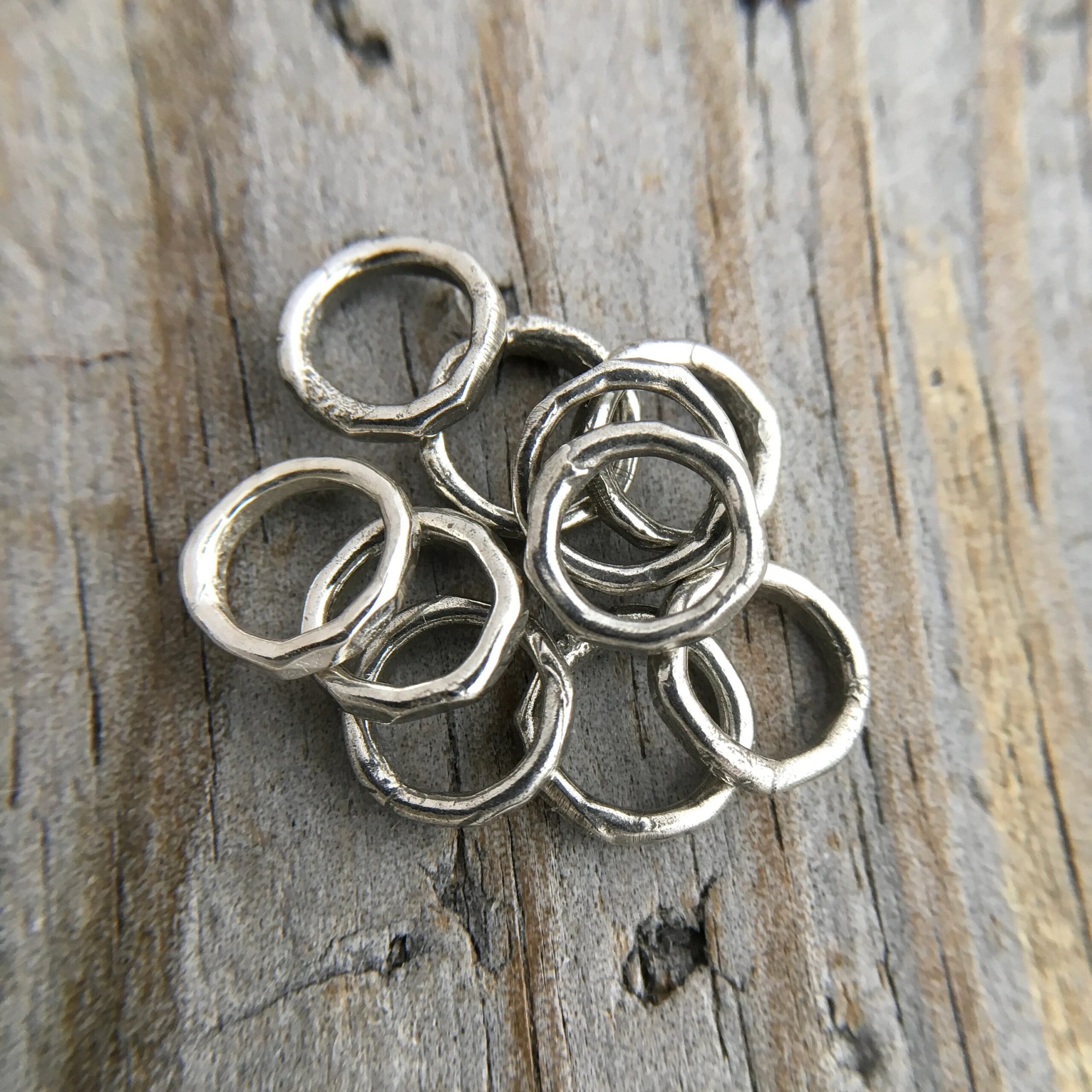 Pile of soldered oxidized jump rings against a wooden background.