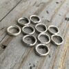 Pile of soldered oxidized jump rings against a wooden background.
