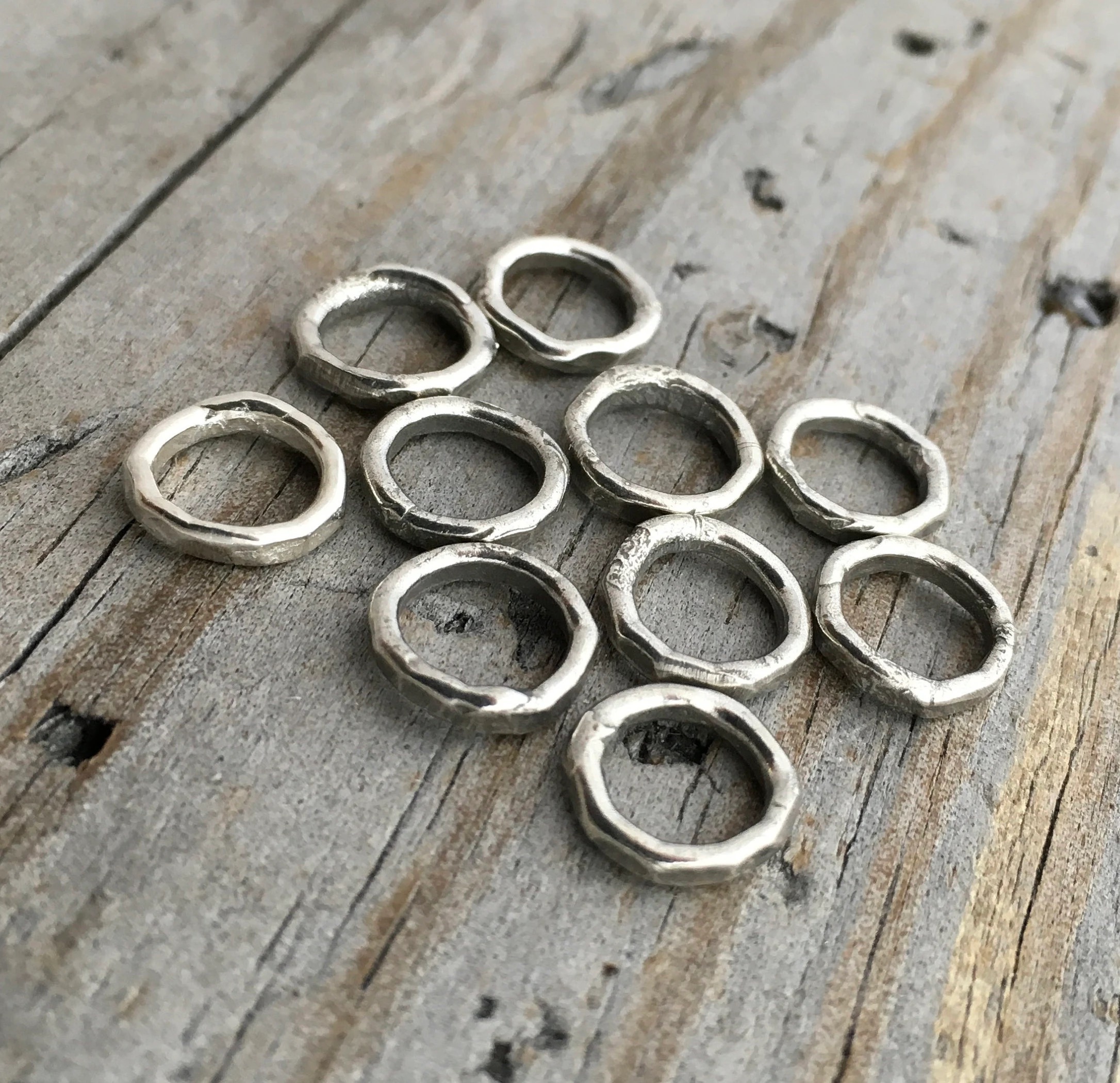 Pile of soldered oxidized jump rings against a wooden background.