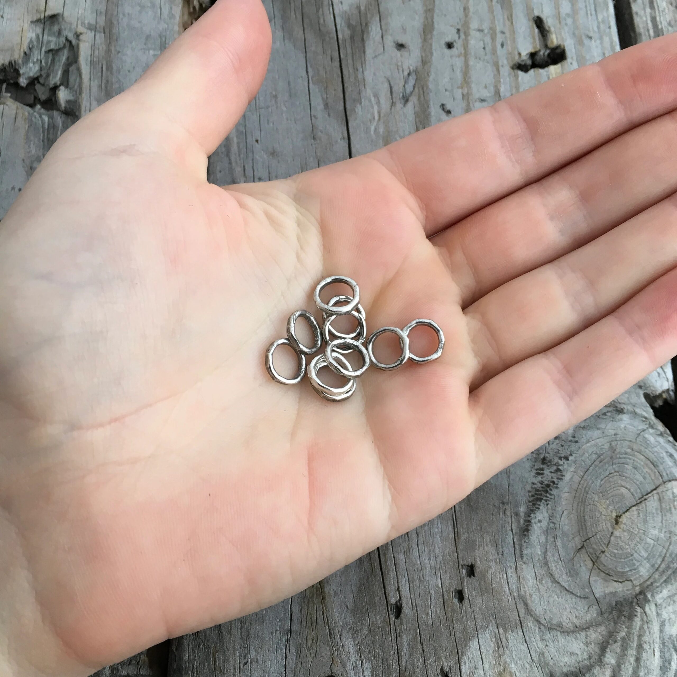 Pile of soldered oxidized jump rings in the palm of a hand.