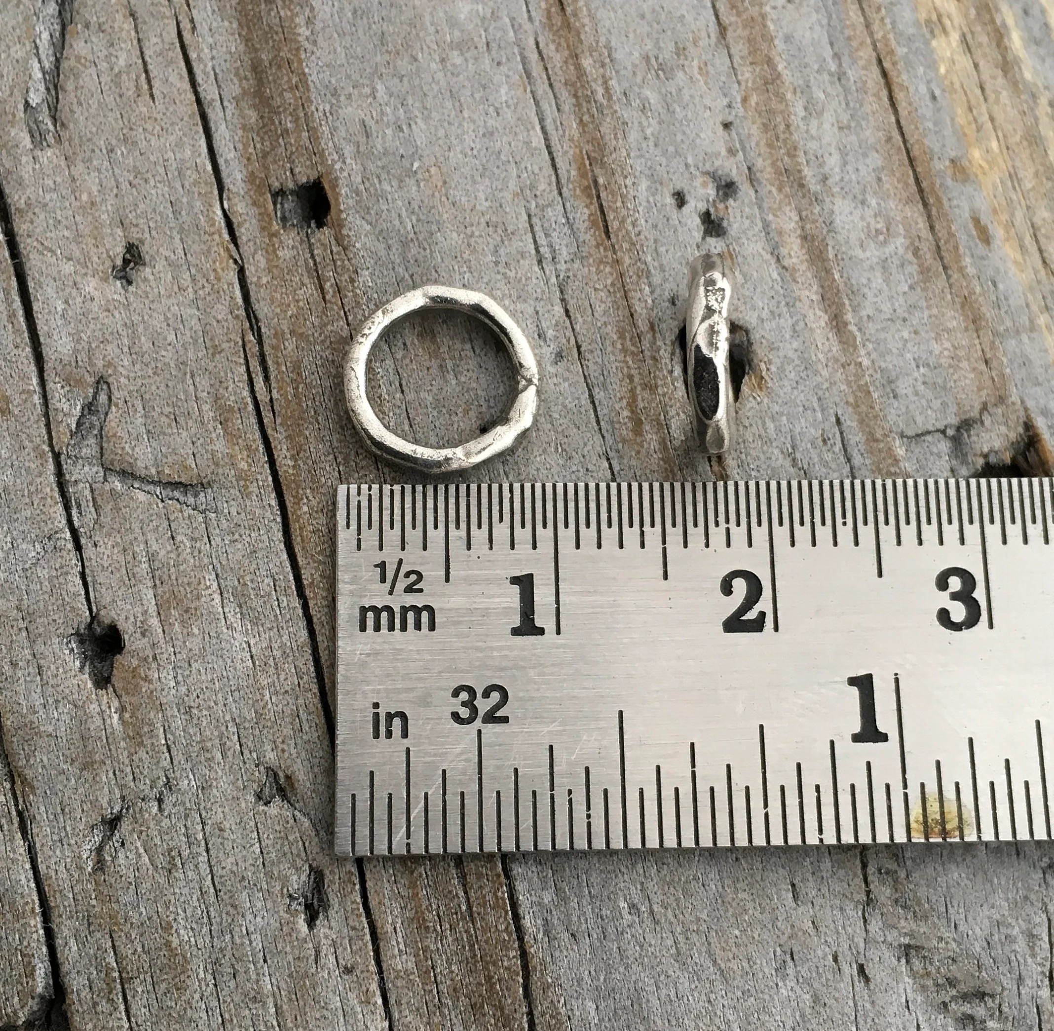 Two soldered oxidized jump rings shown against a ruler to demonstrate size and width.